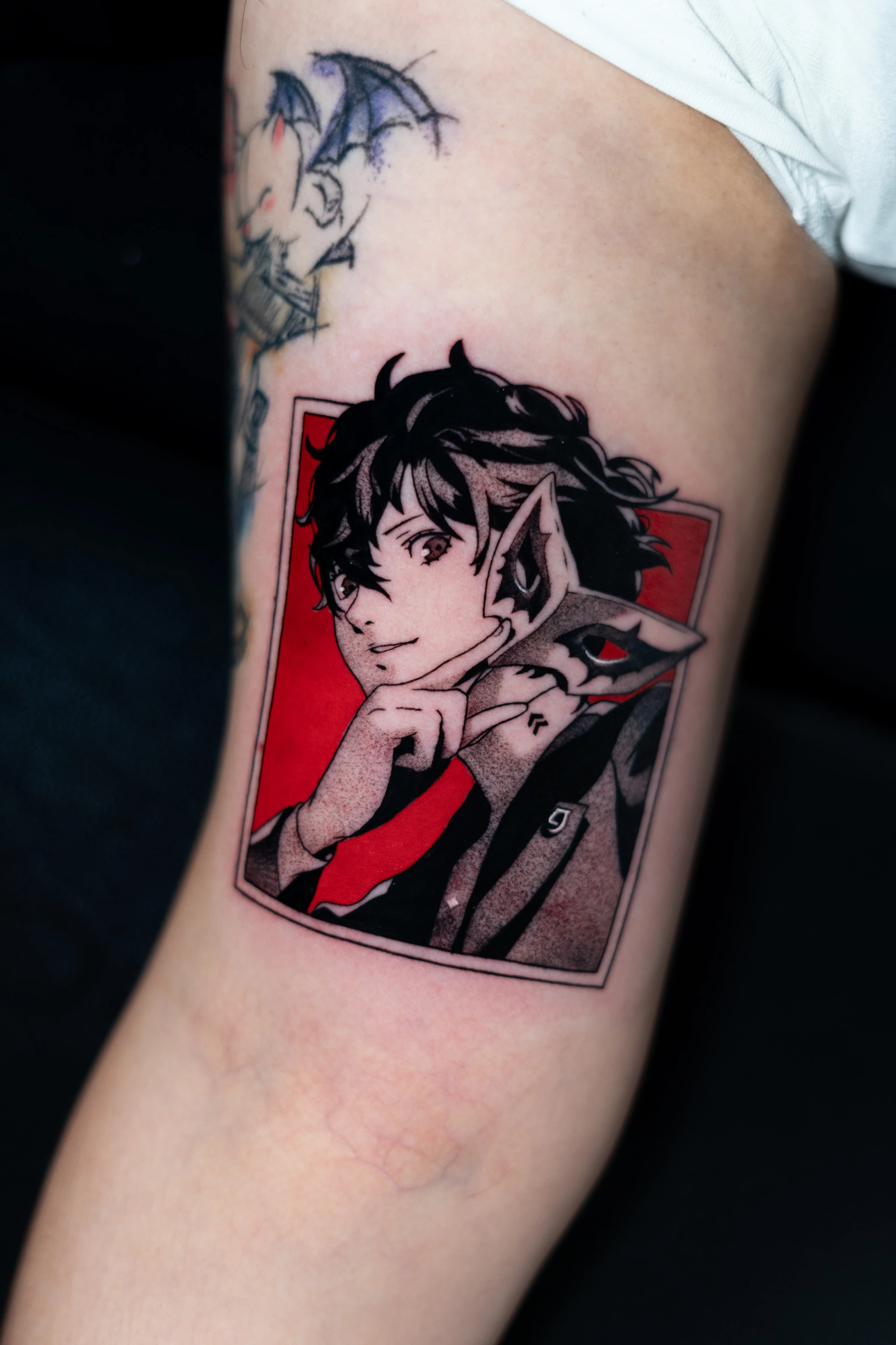 Un tatuaje detallado de una figura con un traje negro y una máscara estilizada sobre un fondo rojo intenso.